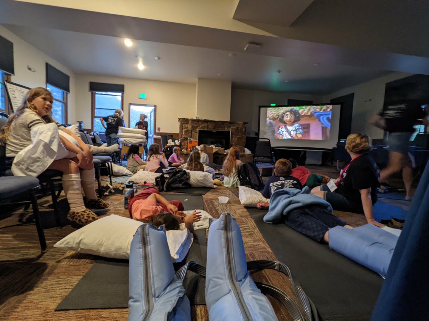 Campers lay on the floor, some using compression pumps, while watching a movie together.