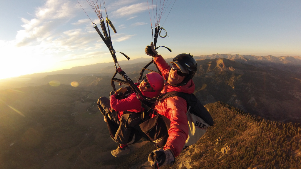 Lindsey Sosovec smiles while parachuting with an instructor over a bright landscape.