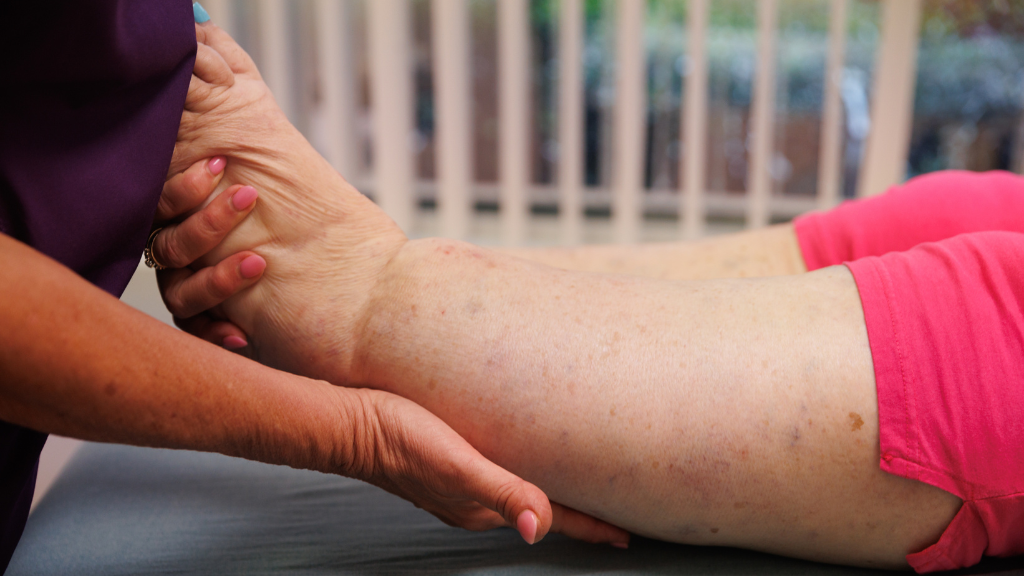A therapist holds a lymphedema patient's foot and leg in their hands in preparation for treatment.